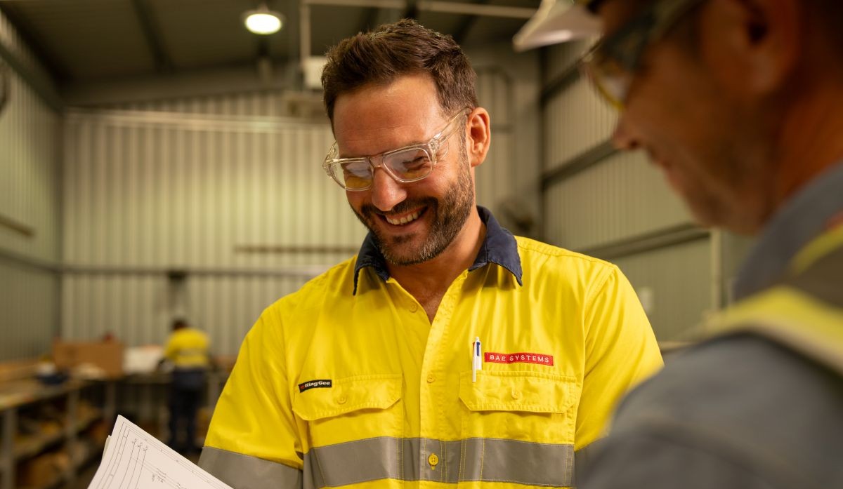 Two men in high vis clothing, standing in a warehouse, having a discussion.