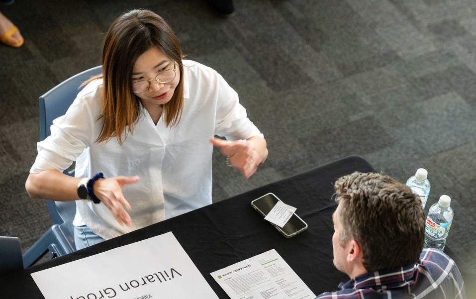 Pictured: An aerial view of a man and a migrant woman sitting across from each other at a table.