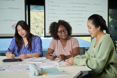 Three women sit at a desk inside an office. 