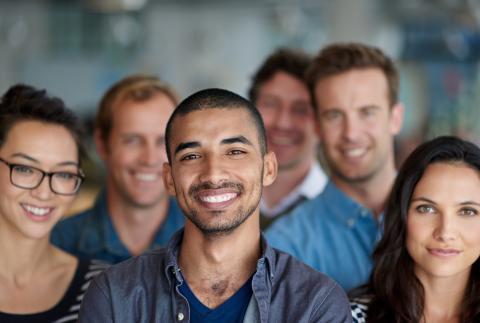 A group of people, mixed genders and races, standing together, smiling at the camera.